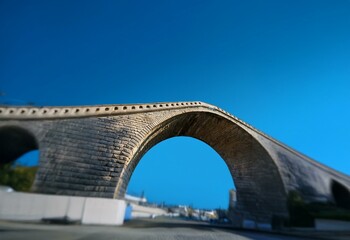 A low angle view of a stone arch bridge against a bright blue sky.