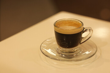 An espresso in a glass is placed on the table. Espresso coffee and saucer with blurred background.