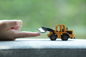 A child's hand touches a toy excavator. Child's hand and toy excavator with blurred background. 