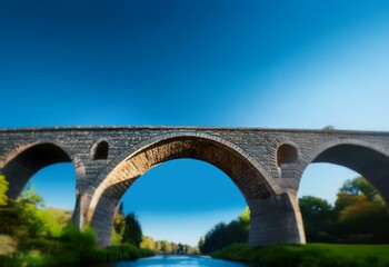 Fototapeta premium An old stone arch bridge spans a river, with a blue sky above.