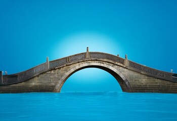Fototapeta premium A stone arch bridge spans a body of water with a clear blue sky in the background.