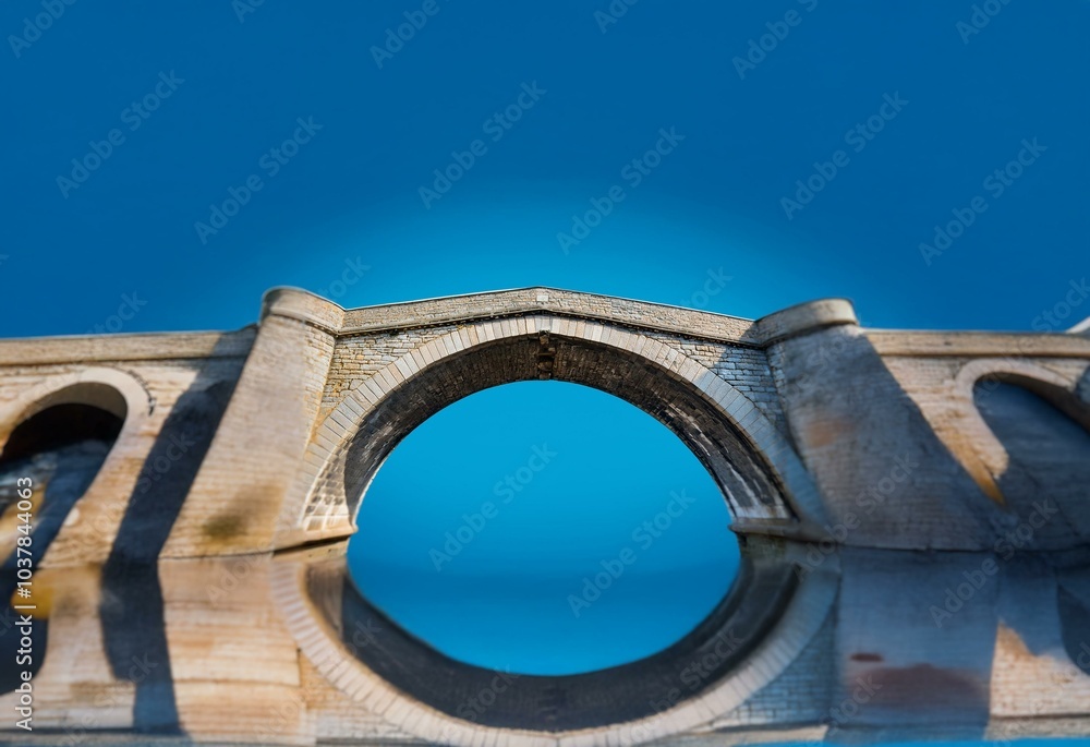 Aufkleber a stone arch bridge with a single arch reflects in the water below, creating a frame for a deep blue