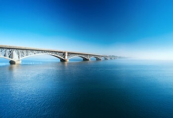 A steel bridge with multiple arches crosses a calm body of water on a clear day.
