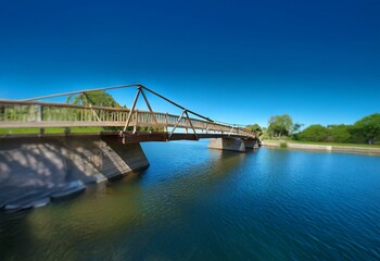 Obraz premium A wooden bridge spans a tranquil body of water with a clear blue sky overhead.