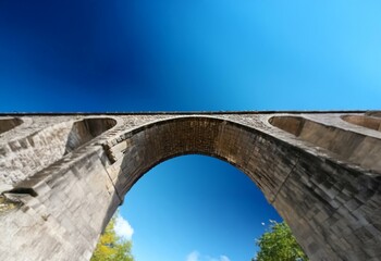 Fototapeta premium A stone archway spans a bright blue sky, viewed from below.