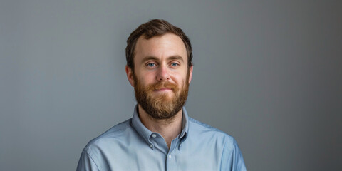 Obraz premium Portrait of a Smiling Man with a Beard in a Light Blue Shirt Against a Gray Background