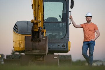 Builder with excavator for construction at the construction site. Machinery tractor with builder at buildings background. Excavator builder worker. Builder with helmet on construction site.