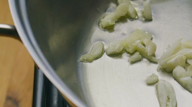Extreme close-up view of minced garlic being added and fried in sizzling olive oil in cooking pan