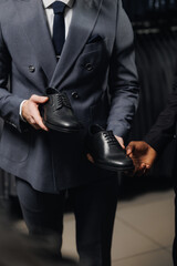 Salesman help for client in mens store. Young African American businessman in suit shopping classic...