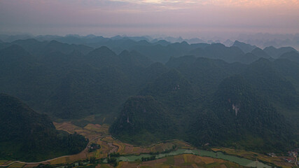 A breathtaking aerial view of a lush green valley surrounded by towering mountains. A winding river cuts through the serene landscape under a clear, expansive sky, creating a sense of natural beauty