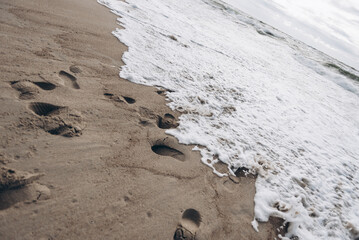 There are several distinct footprints imprinted in the soft sand along the beach that is situated near the vast ocean waters