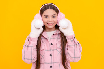 happy kid in fur earmuffs playing snowballs on yellow background, winter