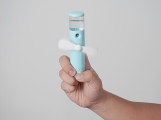 Male person hand holding portable mini mist sprayer fan, over grey