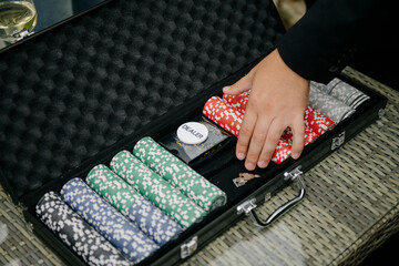 A person is carefully placing various colored poker chips inside a briefcase, making sure they are organized and secure