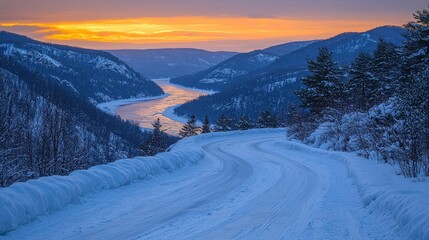 Winding road through snow-covered mountains at sunset, showcasing a tranquil river under an orange sky