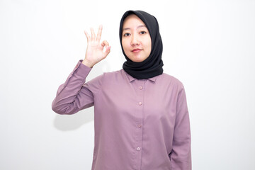 portrait of Indonesian Asian woman wearing shirt and hijab showing ok sign with one hand on eyes looking at camera through fingers. giving sign of agreement. Isolated on white Background