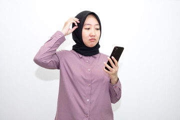 Portrait of Asian, Indonesian woman wearing shirt, hijab and holding mobile phone who is overwhelmed with emotions and bad thoughts, unhappy and stressed. Isolated on white background