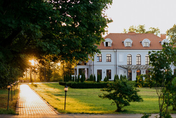 A spacious, large white house featuring a bright red roof is beautifully surrounded by numerous...
