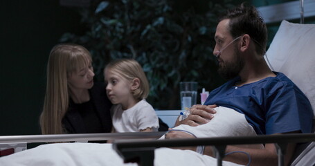 Happy family young man with oxygen tube in nose mother and daughter sit near lovely husband man signs agreement for surgery.