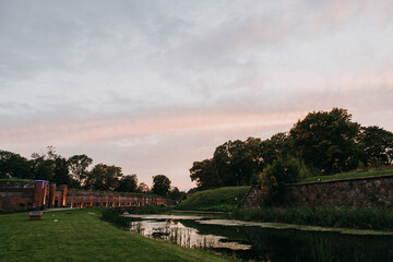 A beautiful river flowing gently surrounded by lush trees and vibrant green grass, all set against a stunning sunset in the background