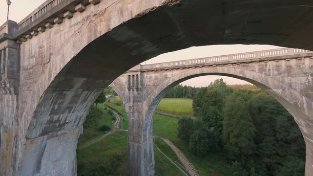 Close-up drone view of stone arches of Stanczyki Bridge in Poland, with green fields and trees visible through structure. Flying through arch of bridge.Bridge at sunset. High quality 4k footage