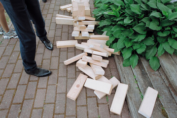 A man is currently standing right next to a large pile of various wooden blocks situated on a sturdy brick sidewalk
