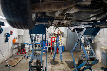 female mechanic standing under lifted car and fixing car in garage