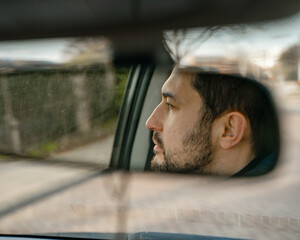 Young man driving a car, reflection in rear mirror