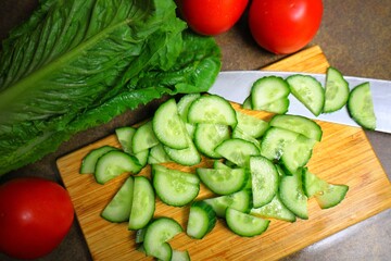 fresh red tomatoes, lettuce leaves, and sliced cucumber on a cutting board