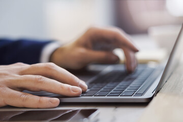 In a close-up shot, male hands are seen typing on the keyboard of a cutting-edge laptop, with an office scene softly blurred in the background.