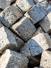 Irregular stacked pile of durable granite paving stones with square shapes, showing the textures and patterns of natural stone, giving a raw rugged look, ideal for construction and landscaping.