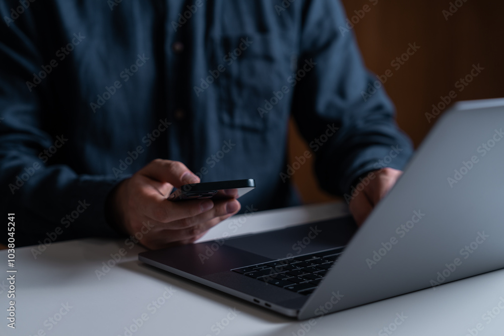 Poster man using smartphone, typing on the laptop keyboard on desk