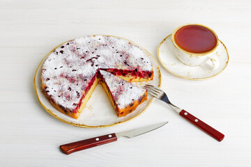 Homemade berry pie with cranberry and cup of tea on white wooden table.