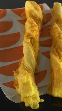 Vertical video social media - Closeup slow dolly shot of two freshly baked, golden, flakey, cheese straws on a takeaway paper packet.