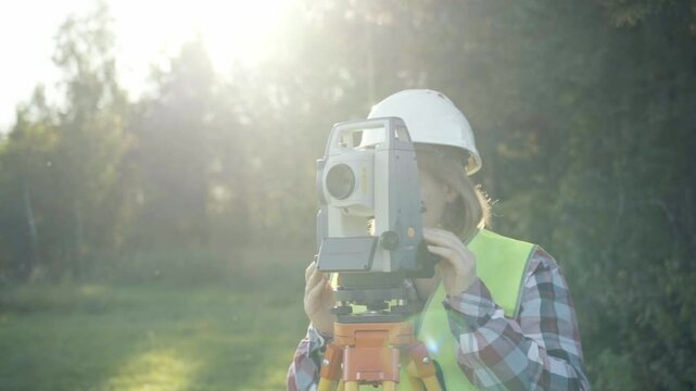 A woman engineer and surveyor performs land surveying work on a sunny day. Concept geodetic work, topography, land surveying, cadastral work.