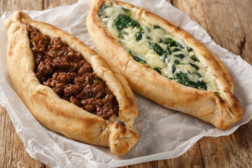 Traditional turkish baked dish pide with ground meat, cheese, spinach and spicy close-up on wooden board on table. Horizontal