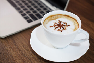 A hot of Latte art coffee with laptop on table at cafe