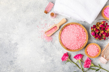 Sea salt for bath with aroma and rose flowers on textured wooden background. Pink sea salt. Spa treatments. Natural salt with herbs and essential oils. skincare concept. Meso for text. Copy space