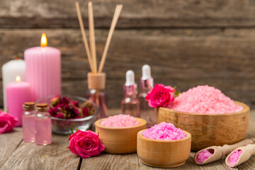 Sea salt for bath with aroma and rose flowers on textured wooden background. Pink sea salt. Spa treatments. Natural salt with herbs and essential oils. skincare concept. Meso for text. Copy space