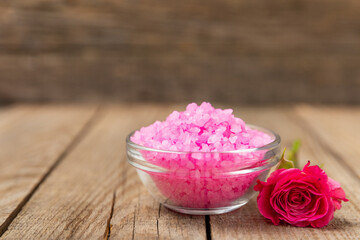 Sea salt for bath with aroma and rose flowers on textured wooden background. Pink sea salt. Spa treatments. Natural salt with herbs and essential oils. skincare concept. Meso for text. Copy space