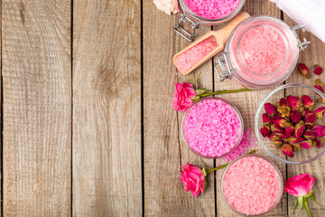 Sea salt for bath with aroma and rose flowers on textured wooden background. Pink sea salt. Spa treatments. Natural salt with herbs and essential oils. skincare concept. Meso for text. Copy space