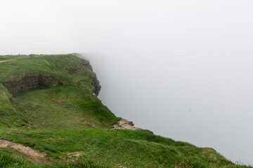 Cliffs of Moher in County Clare, Ireland, reveals a grassy cliff edge fading into the dense mist....