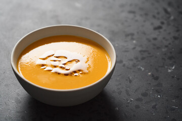 Pumpkin soup decorated with herbs and olive oil in white bowl on concrete background with copy space