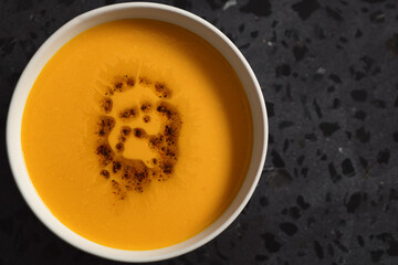 Pumpkin soup decorated with herbs and olive oil in white bowl on concrete background with copy space