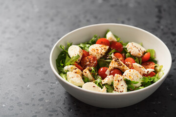 Salad with cherry tomatoes, mozzarella and frisee leaves in white bowl on concrete background