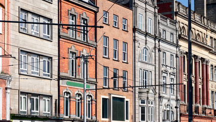 Facades of various buildings in Dublin, showcasing a contrast of red brick and stone architecture. The image highlights the urban character of the city, with the tram lines crossing in front