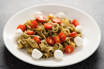 fettuccine with pesto, tomatoes and mozzarella on white plate