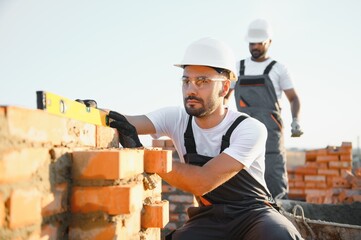 Builders work at the construction site in overalls and helmets. Construction of a brick wall....