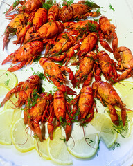 Many red boiled crayfish in a plate on the table with lemon slices.