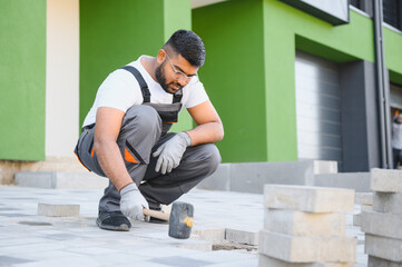 Indian Worker skillfully laying paving stones using a hammer and wearing gloves, showcasing precision